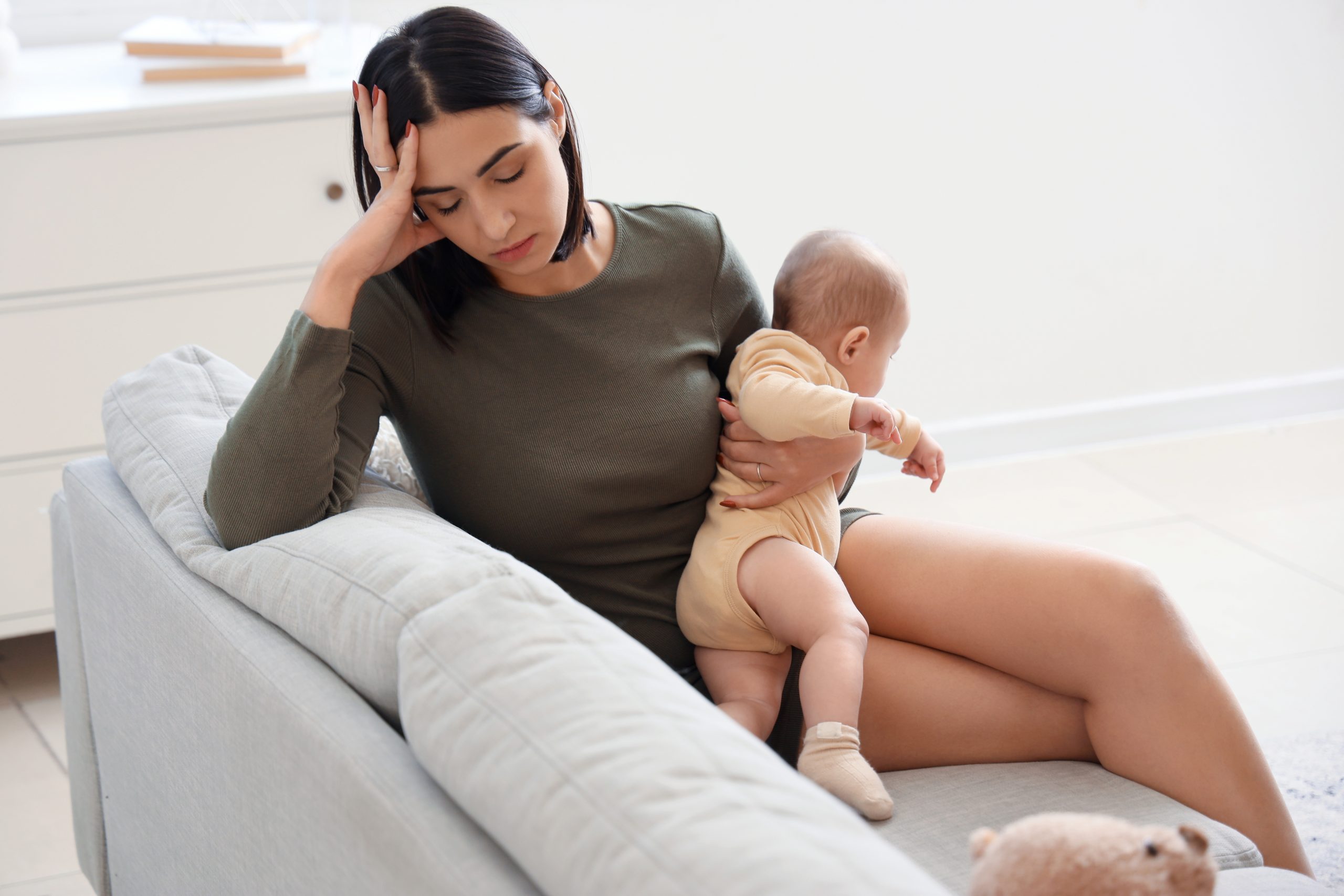 Young woman with her baby suffering from post-partum depression on sofa at home